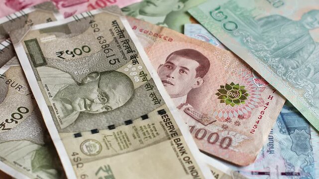 Indian 500 rupee banknotes (INR) are falling on top of Thailand national currency (THB). Paper cash lands across colorful Thai baht, illustrating overseas remittances, global trade and personal wealth