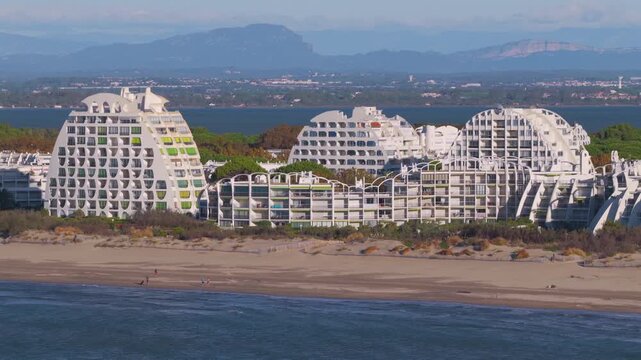 Aerial parallax view of Petite Motte beachfront apartments in La Grande-Motte with Pic Saint-Loup and Montpellier in background, France
