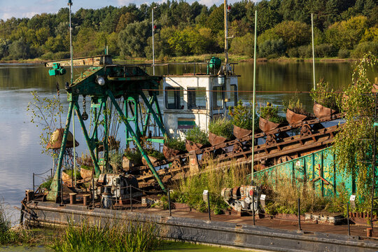 View of an abandoned, rusted dredging vessel overgrown with wild vegetation and small trees on the Nemunas River in Zapyskio seniunija, Kauno apskritis, Lithuania.