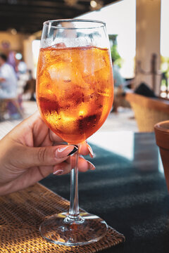 View of a refreshing Aperol Spritz cocktail held in a hand at Kimpton Mas Olas Resort And Spa with a blurred outdoor patio setting in El Pescadero, Baja California Sur, Mexico.