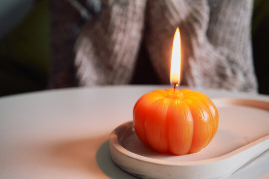Person relaxing at home beside glowing pumpkin candle