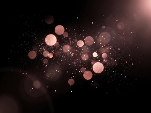 Rose gold bokeh lights with shimmering dust particles on black background, elegant pink glitter sparkles and magical lens flare for festive celebration