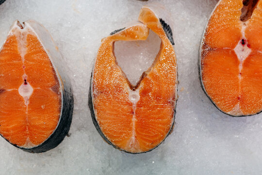Frozen salmon steaks and raw red fish displayed on ice for seafood retail sale at fish market, offering nutritious protein rich ingredients for healthy meals and home cooking.