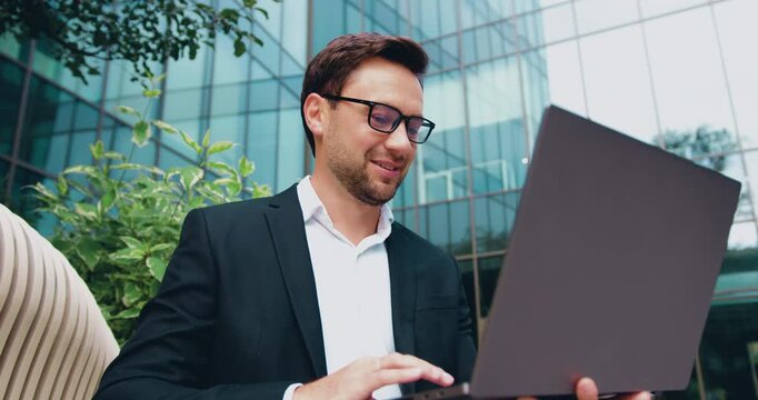 Bearded businessman taking part in an online business meeting on a laptop outdoors, remote work and digital communication concept
