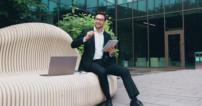 Businessman analyzing financial data on a tablet while standing outdoors near a modern office building. Modern business, digital technology, and corporate communication concept