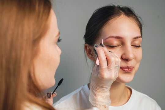 Eyebrow shaping session with cosmetologist wearing gloves performing precise grooming on relaxed young woman, closeup studio portrait showing facial expression