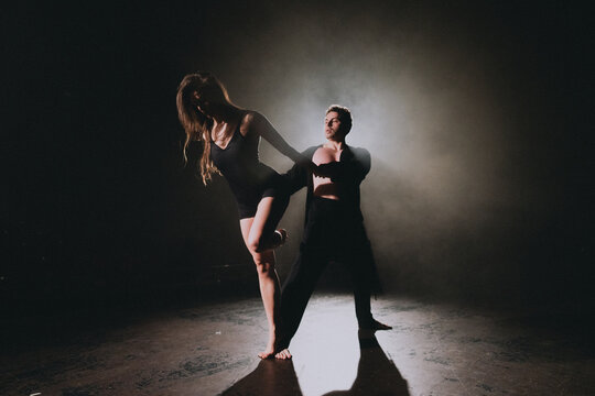 Contemporary dance partners performing dramatic backlit lift on dim smoky stage with expressive pose and shadowed floor scene to convey strength and grace in