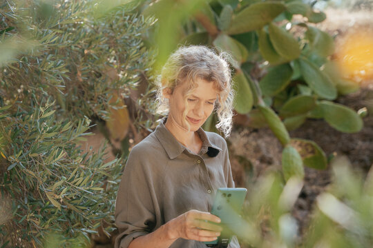 Blonde Woman Using Smartphone for Outdoor Content Creation in Sunny Garden