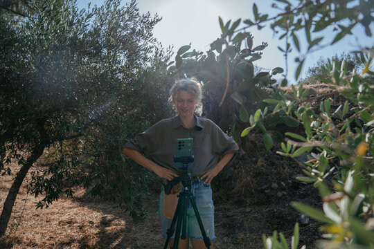 Female Content Creator Smiling at Smartphone Camera on Tripod in Mediterranean Garden