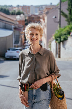 Smiling Blonde Woman with Gardening Tools and Wicker Basket on Village Street