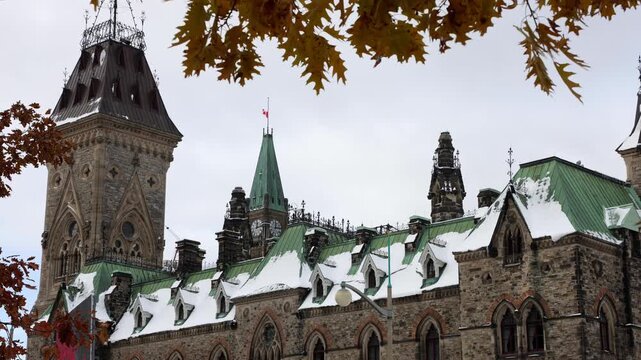 West Block Parliament building with snow covered roofs framed by fall foliage