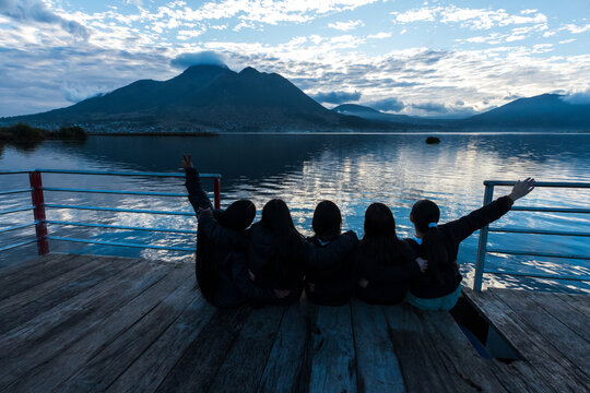 Group of young female friends enjoying the scenic view of San Pablo Lake and Imbabura Volcano from a wooden pier in Otavalo, Ecuador