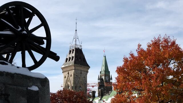 Canadian Parliament Hill building and Peace Tower viewed behind historic cannon statue in Ottawa. Historic tower and autumn foliage