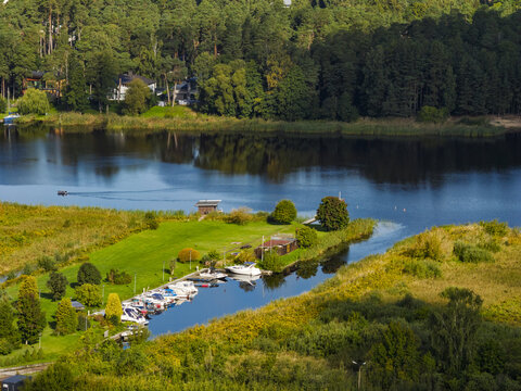 Aerial view of Ragakapa Nature Park featuring a small marina with docked boats in a narrow inlet surrounded by lush green forests and wetlands in Jurmala, Latvia.