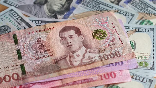 Thailand baht (THB) banknotes are placed on top of 100 US dollar (USD) bills. Concept of exchange rate, global finance, and international economy. Real time footage