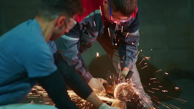 Two workers grind metal, sparks flying around them. One man wears goggles, the other a red helmet. They focus, adjusting the grinder with care. Their teamwork shows skill and precision