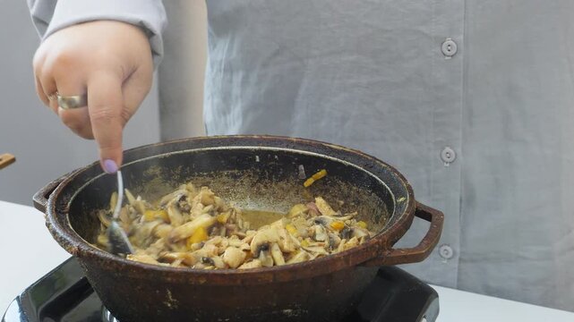 In a deep cast-iron skillet, onions and chicken are simmered in a sauce and spices with mushrooms and tomatoes. Medium shot.