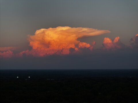 Aerial view of a large, golden-lit cumulonimbus cloud illuminated by the setting sun above a dark, silhouetted landscape in Loveland, OH, United States.