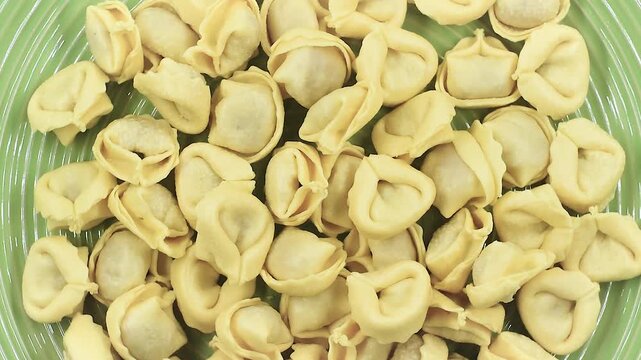 fresh uncooked tortellini filled with prosciutto crudo and parmesan cheese, close-up on a green plate, rotating video