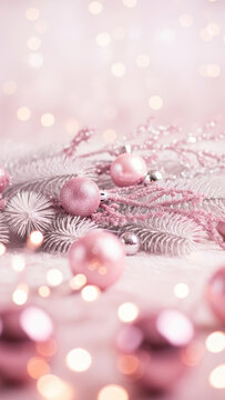 Pink glitter Christmas ornaments on white frosted pine branches with pink bead garland and bokeh lights background