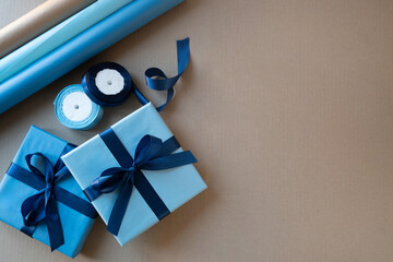 Two blue gift boxes with navy satin bows and wrapping supplies arranged on kraft paper. Flat lay with large copy space for holiday promotion, birthday greetings and advertising. © svetlana_cherruty
