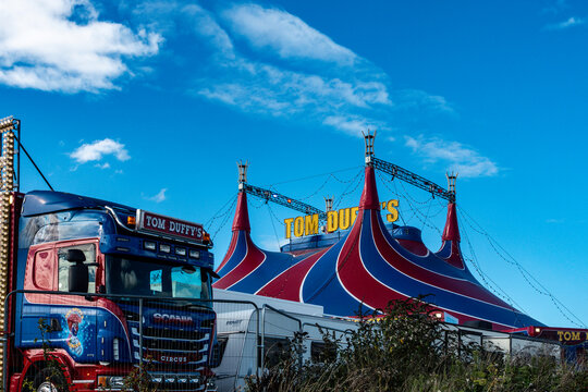 Tom Duffy's Circus big top tent and transport truck stand behind security fencing under a blue sky in Dublin, Ireland.
