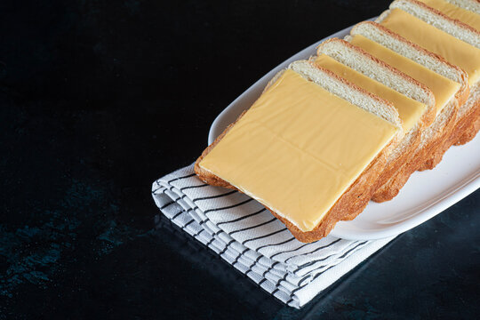 Open-faced cheese sandwiches on a white plate with a striped kitchen towel against a dark background. Sliced bread and cheese for breakfast menus, snack advertising and food banners with copy space.