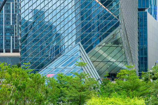 Glass building with reflective modern facades and green trees in Shenzhen city, China. Geometric architecture, urban greenery, contemporary design, green city development, landscape integration