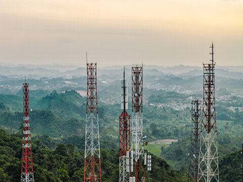Aerial view of television broadcasting station with tall metal communication towers set against rolling green hills and a hazy sky in Samarinda, East Kalimantan, Indonesia.