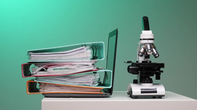Scientist in a lab coat carries a tall stack of binders beside a desk with laptop and microscope, illustrating the merge of paperwork and digital research in modern science