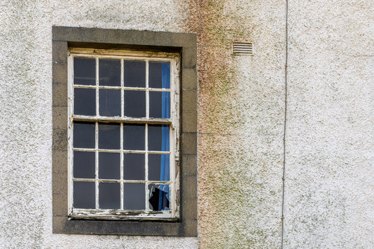 Derelict sash window with peeling paint on weathered render wall