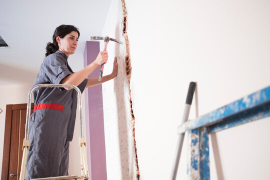 woman working at home with mansonry and renovation. Chopping the wall with a chopper hammer