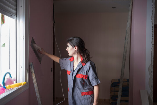 woman working at home with mansonry and renovation, Uniforming the wall paste with the flat tool