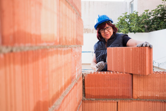 mature woman bricklayer lays bricks in the construction and remodeling of the terrace room of a house
