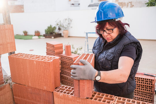 mature woman bricklayer lays bricks in the construction and remodeling of the terrace room of a house