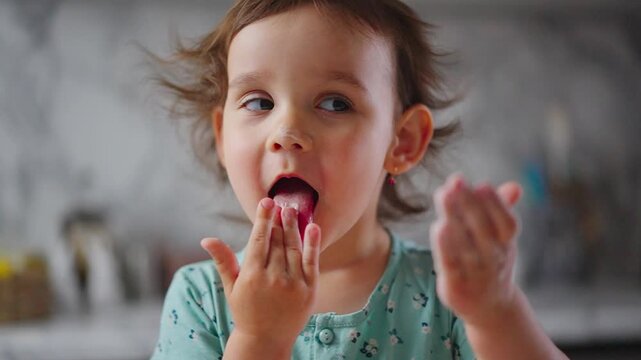 Curious child enjoys a sweet, colorful treat. Child's eyes sparkle with delight. Hands hold the candy, ready to eat. Perfect for family, food, or playful moments. Natural kitchen backdrop