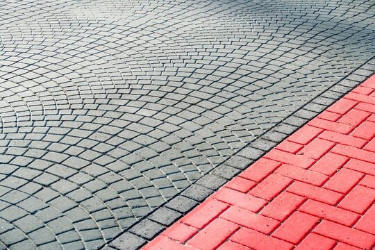 Curved gray cobblestone pavement beside red brick paving. Urban ground surface. Road and walkway construction. Geometric paving pattern and textured street background.