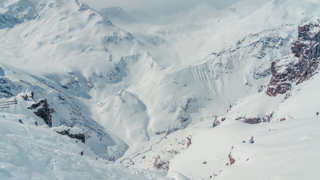 Panoramic snow-covered Caucasus mountain valley with steep ridges and rocky outcrops, tranquil winter landscape