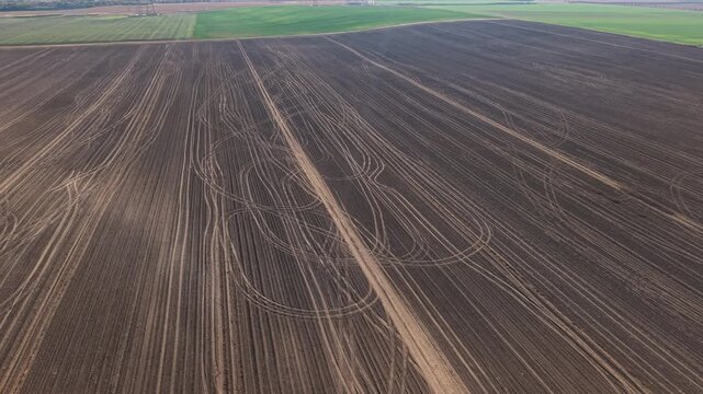 Aerial drone view reveals tractor tire tracks crossing freshly plowed agricultural field in rural Germany. Curving wheel marks intersect parallel soil furrows, creating abstract geometric patterns