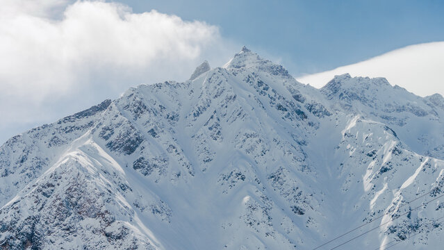 Mount Elbrus summit and snowy Caucasus ridges under pale blue sky with textured cornices and steep slopes