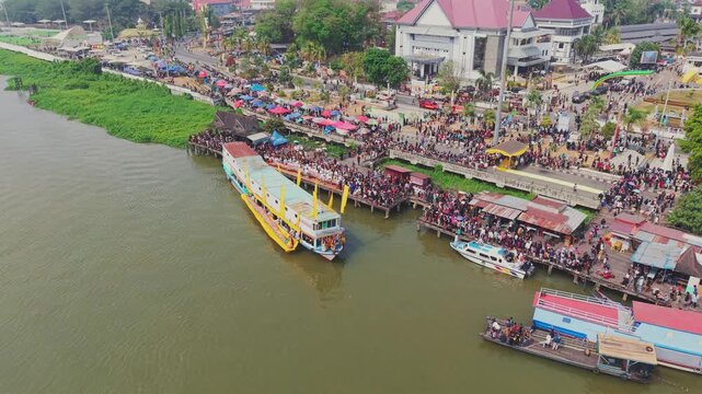 Tenggarong, Indonesia - 27 September 2026: Aerial view of the Ngulur Naga Erau festival on the Mahakam River with traditional boats and crowds gathered along the waterfront.
