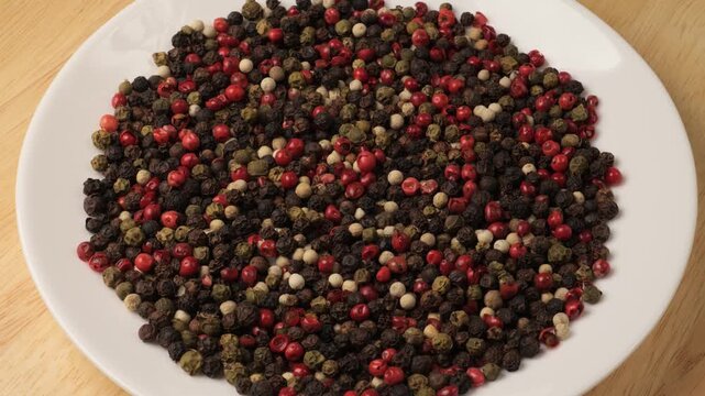 Mixed peppercorns rotating on a white plate