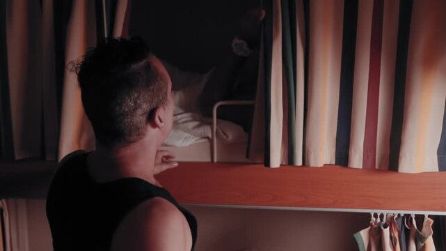 Man going to sleep in a bunk bed inside a small, shared cabin on a cruise ship after work