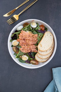Healthy salad with grilled salmon, bread, and assorted vegetables on a dark surface