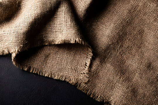 A napkin in the shape of old burlap fabric, placed on a sackcloth table, viewed from above