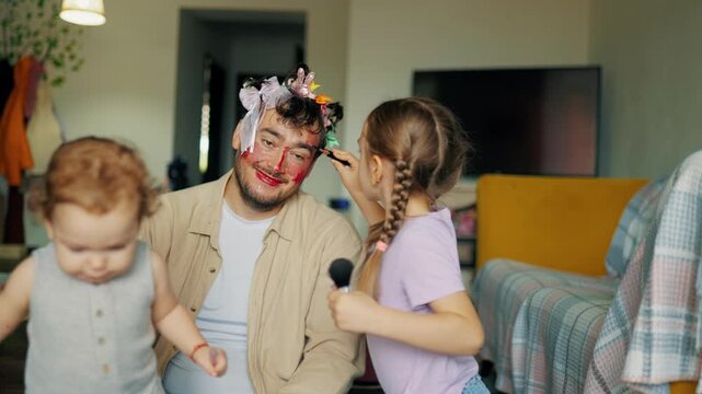 Young sisters playing pretend beauty salon decorating father face. Creative child development