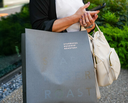 Tokyo, Japan - October 12, 2026: Customer Holds Starbucks Reserve Roastery Shopping Bag While Using Smartphone