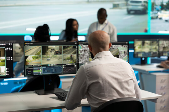 Traffic control, surveillance and camera feeds as operator checks road displays with coworkers nearby. Transport safety, urban mobility and monitoring support city traffic oversight in control room.