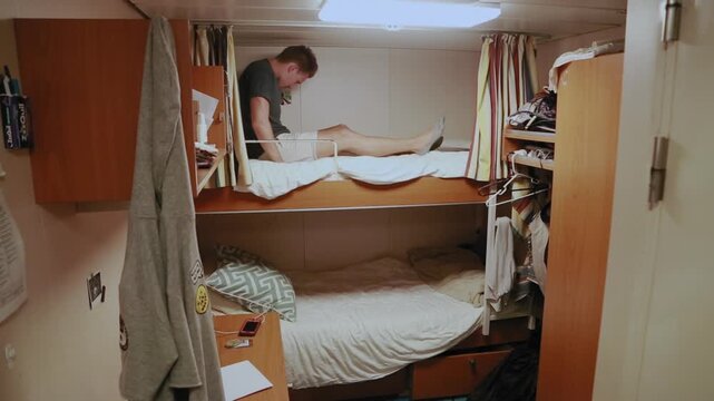 Young man climbing into his bunk bed in a small cabin on a cruise ship to go to sleep