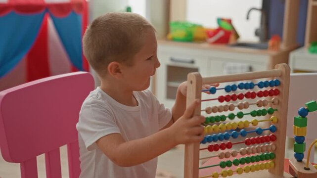 Boy lifts a colorful wooden abacus above his head while seated at a table in a playroom inside a building; frustration and play.